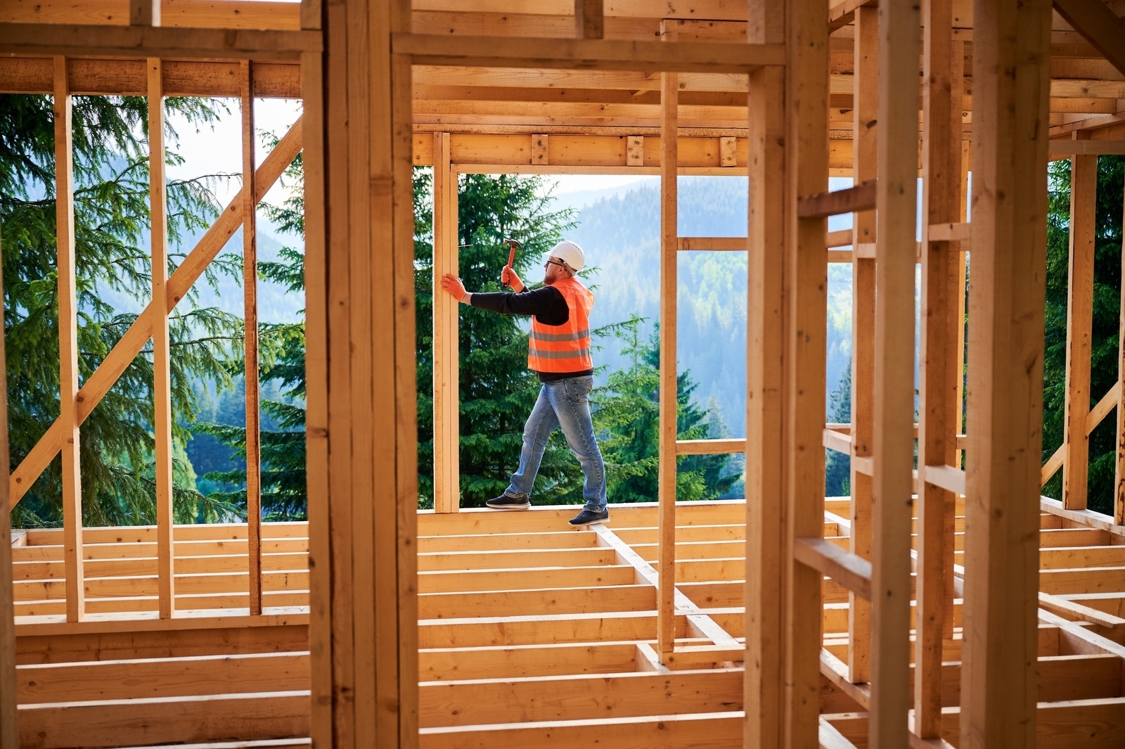 Carpenterconstructingtwo storywoodenframehousenearforest manhammering | construction spike Carpenterconstructingtwo storywoodenframehousenearforestmanhammering