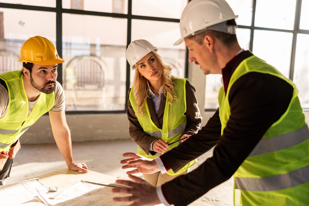 Threeworkersinsafetygeargatheraroundatablewith | construction spike Threeworkersinsafetygeargatheraroundatablewith